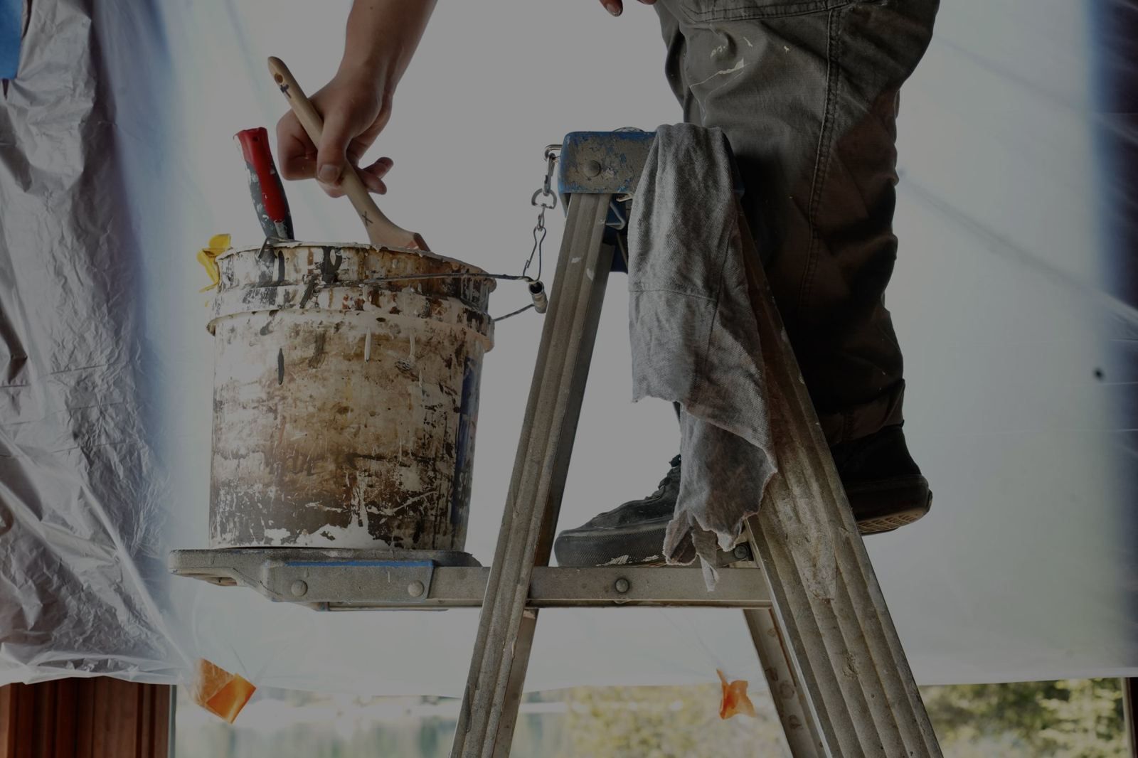 A painter loading a brush from a bucket on a ladder