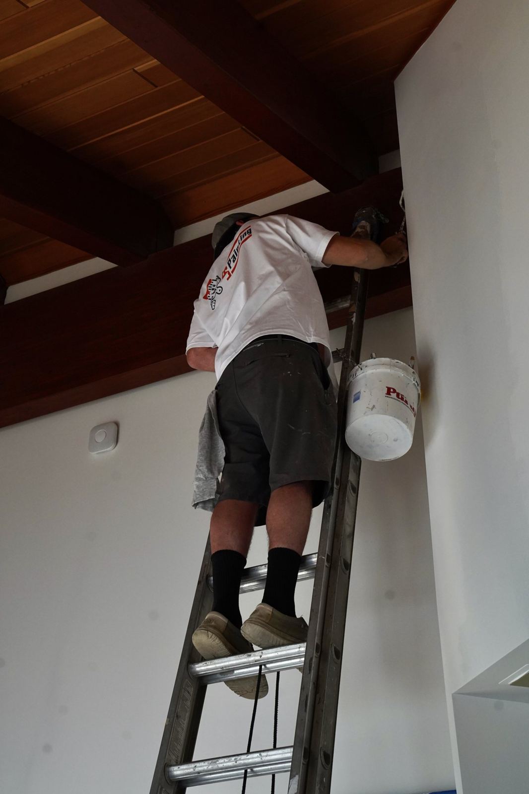 A painter working a high wall from a ladder