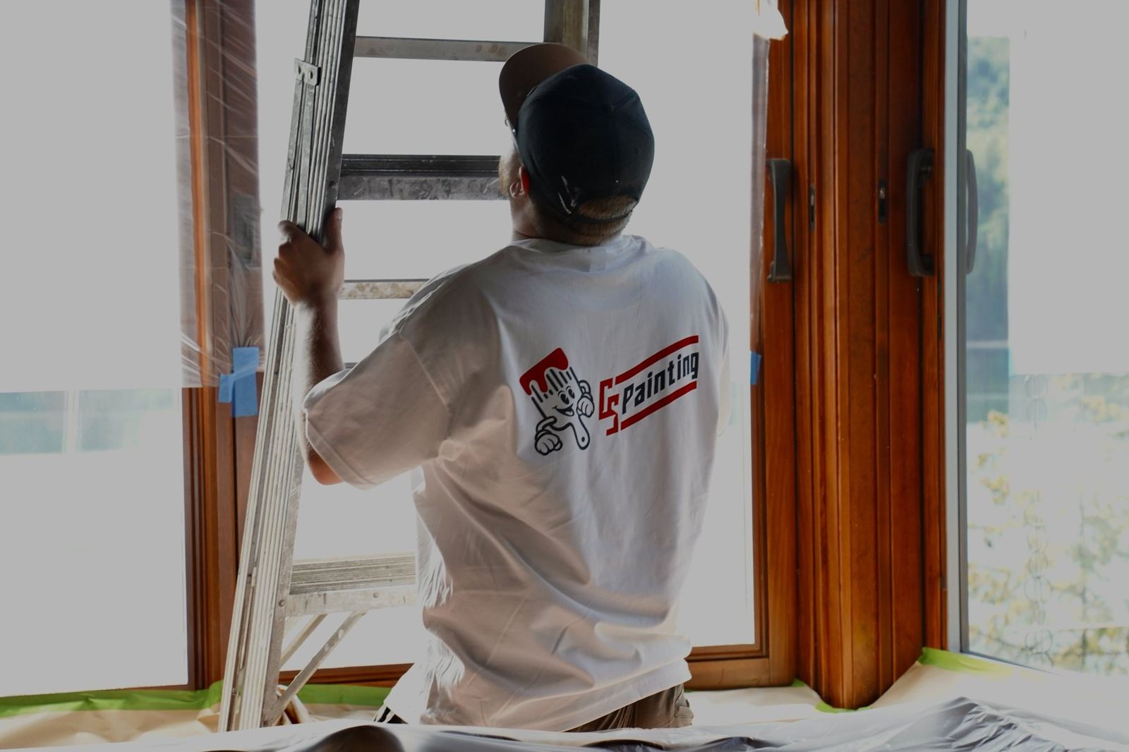 A CS Painting crew member setting a ladder at a wood-trimmed window